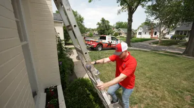 Técnico de Mighty Dog Roofing colocando una escalera para inspeccionar el tejado de una vivienda suburbana en Sarasota. Cerca hay aparcada una camioneta con el logotipo de Mighty Dog.
