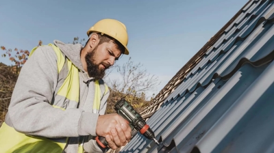 hombre con casco trabajando en un tejado con una herramienta eléctrica