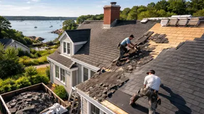 Realistic photo of Rhode Island roofing contractors removing old shingles and installing new dark gray shingles on a coastal home during a roof replacement, showing proper tear-off before re-roofing to prevent ice dams and ensure warranty compliance.