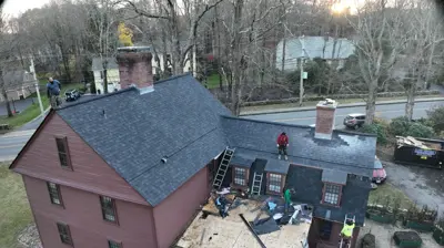 Drone view of a historic estate property in Smithfield, Rhode Island with multiple roof sections including architectural shingles and cedar shake dormers.