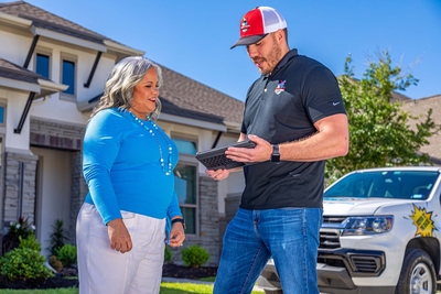 Un contratista de Mighty Dog Roofing discutiendo los detalles de la inspección del tejado con un cliente fuera de su casa.