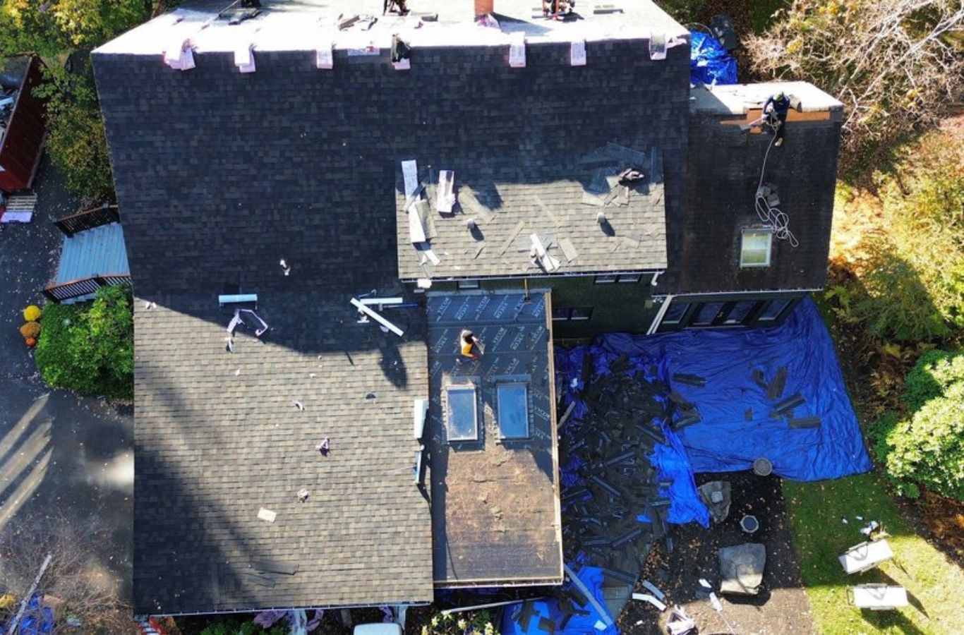 Dos miembros del equipo de Mighty Dog Roofing instalando tejas en un tejado en Acton, MA, ilustrando las ventajas de contratar a una empresa profesional de tejados.