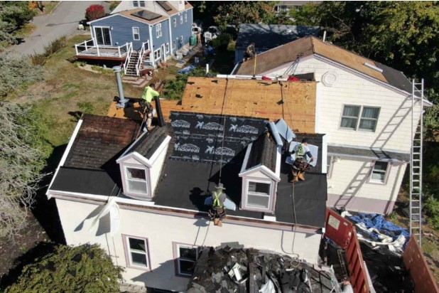 Un miembro del equipo de techado coloca tejas en una casa de Harvard, MA, con precisión y cuidado.