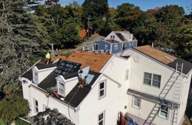 Un técnico de techos de Mighty Dog Roofing aplicando tejas en Stow, MA, destacando el servicio profesional.